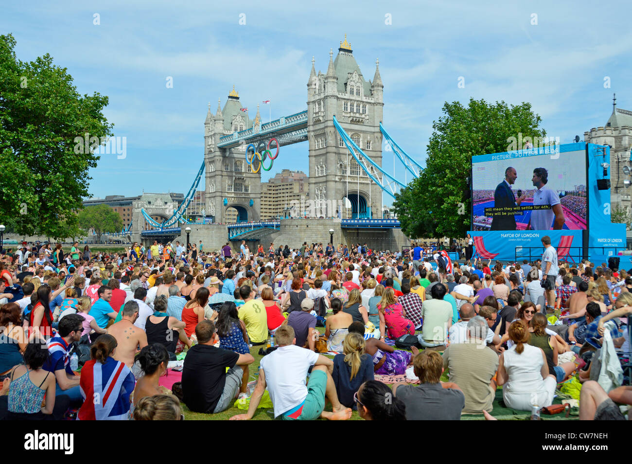 Menschenmenge sitzt auf dem Rasen und schaut sich die Olympischen Spiele 2012 in London an TV Sport Event großen Outdoor-TV-Bildschirm in Potters Felder Park Southwark England Großbritannien Stockfoto