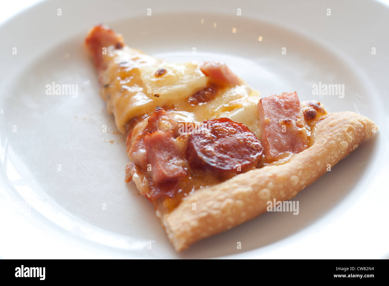 Pizza mit Wurst, Schinken, Hühnerfleisch, Paprika, Ananas auf einem weißen Teller. Stockfoto