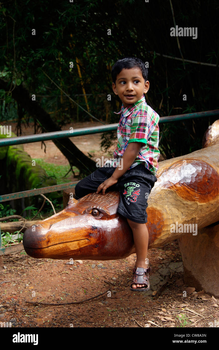 Kleiner Junge genießt sitzen auf der Krokodil geformten Holzbank im Zoo von Trivandrum in Kerala in Indien Stockfoto