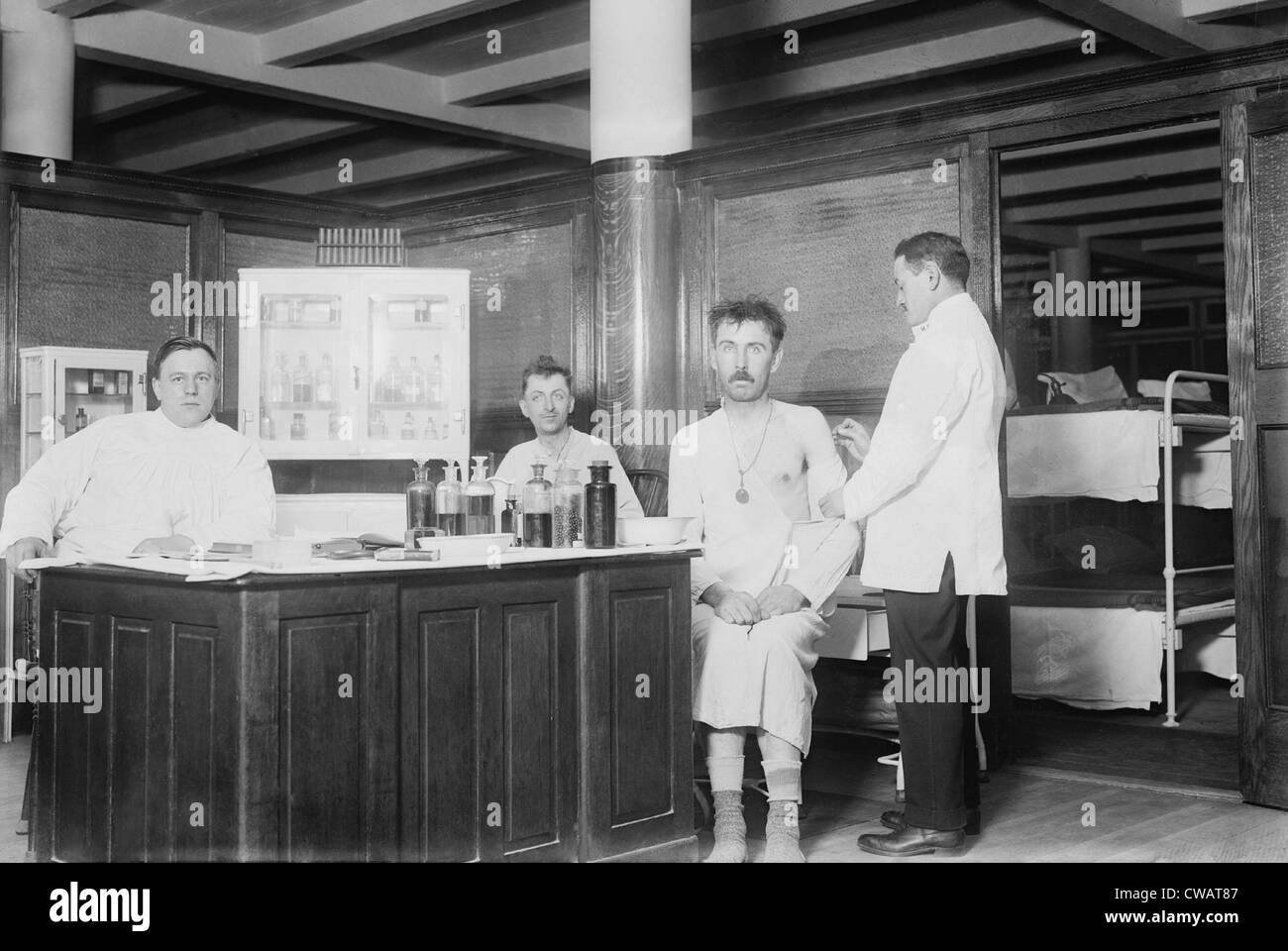 Zwei vor kurzem gebadet Männer werden vom Arzt in New York City Unterkunft Gemeindehaus Impfungen gegeben. Ca. 1910. Stockfoto