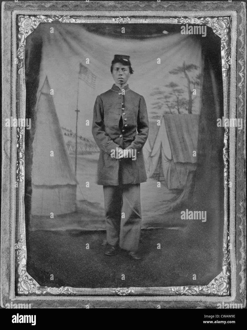 Afrikanische amerikanischer Soldat stellte vor malerischen Studio Kulisse der Zelte in einem Militärlager mit einem prominenten US-Flagge. Die Stockfoto