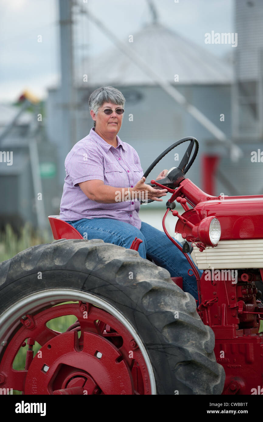 Frau Bauer Reiten Traktor vor Ackerland vor Scheunen und silos Stockfoto