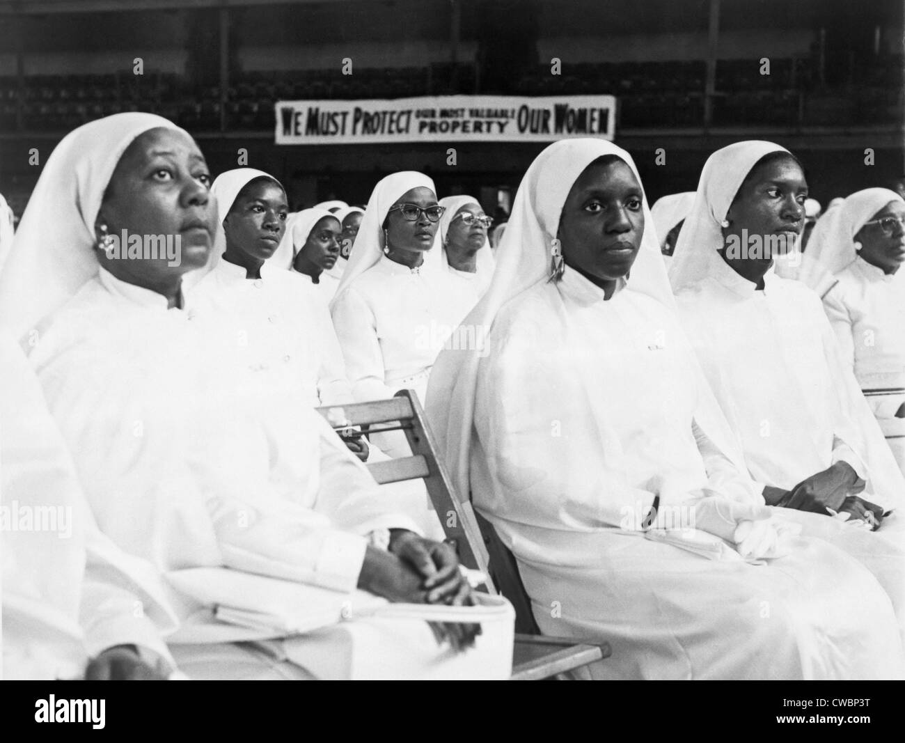 African American Frauen gekleidet in weiß auf einer Nation of Islam-Tagung in New York City.  Hinter den Frauen ein Zeichen liest, "Wir müssen Stockfoto