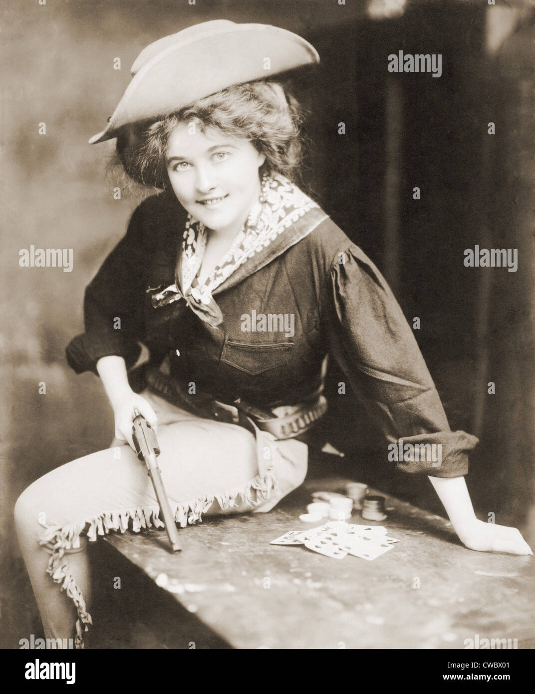 Wende des Jahrhunderts Cowgirl Holding Revolver, sitzt auf einem Tisch, mit Spielkarten und Chips. Ca. 1900. Stockfoto