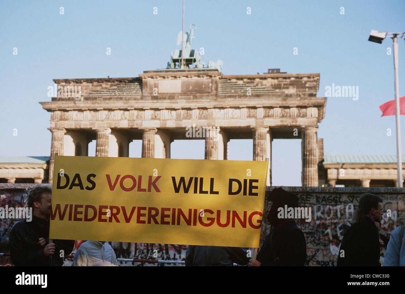 Westdeutsche Bürger zeigt einen Banner, die Menschen werden WIEDERVEREINT, während sie darauf, für den Abriss der Berliner Mauer am warten die Stockfoto