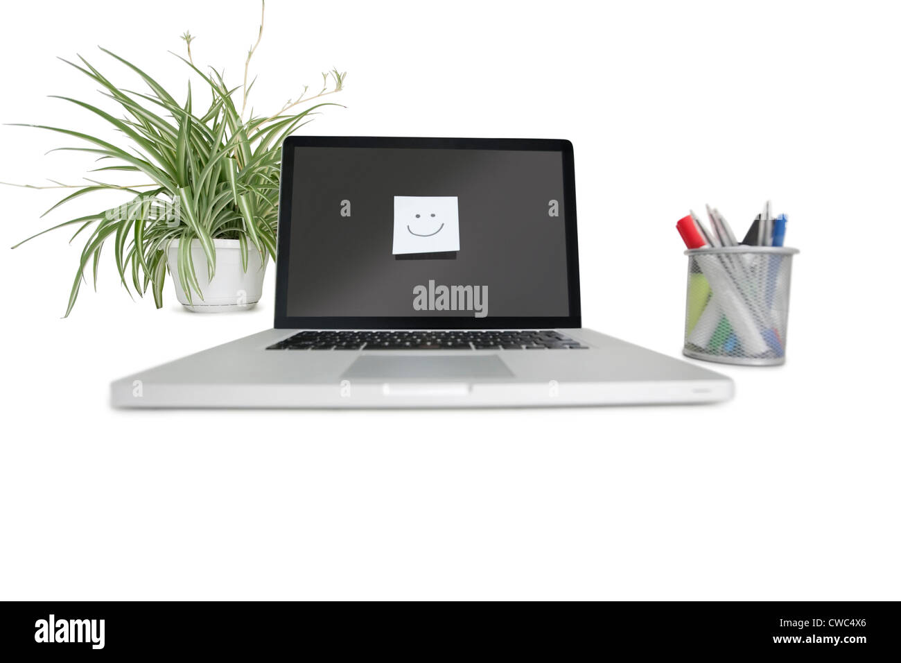 Smiley-Gesicht-Notiz auf Laptop mit Büromaterial und Topfpflanze Stockfoto