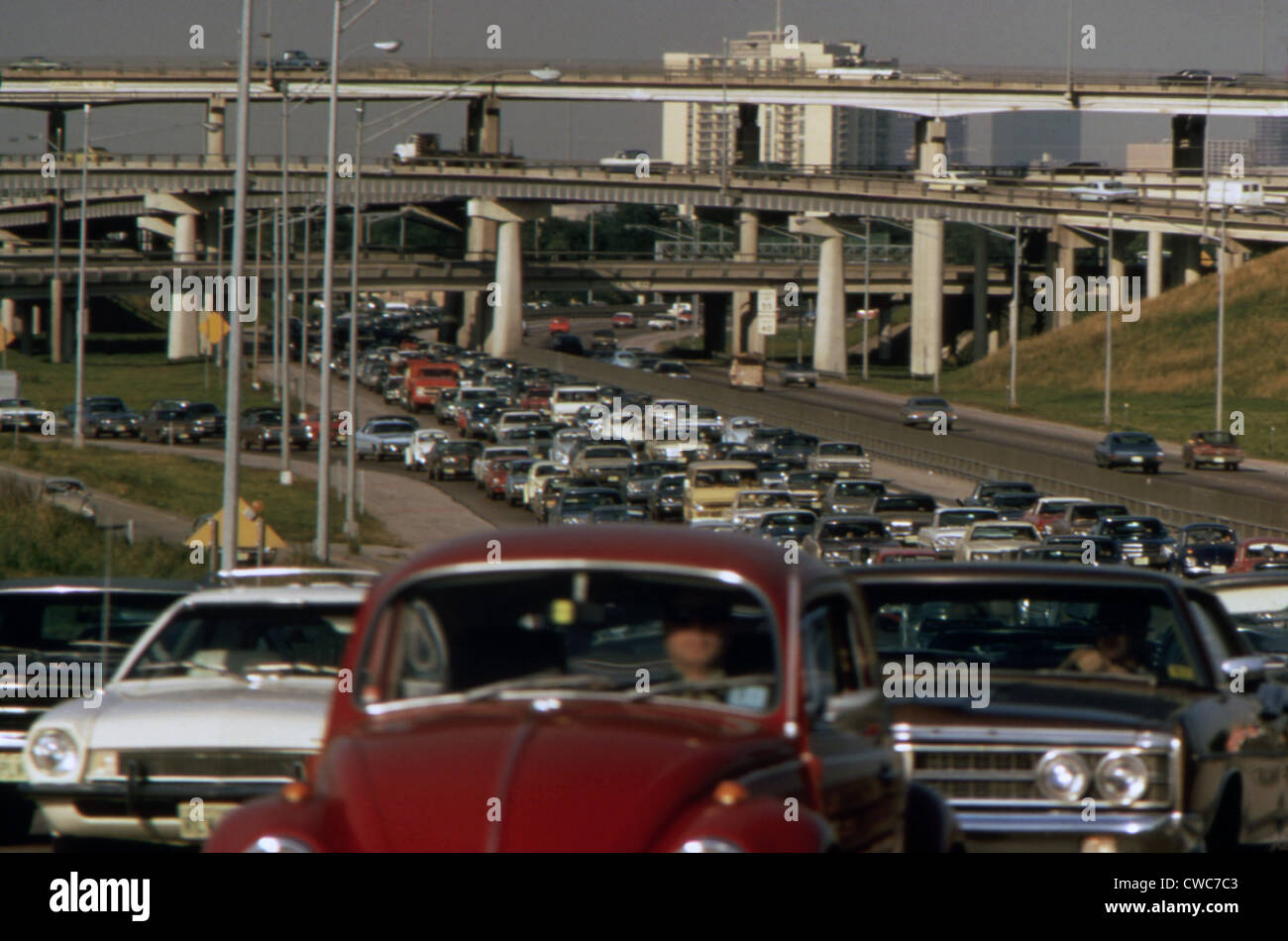 Stau auf der Autobahn mit einer mehrstöckigen Gruppe von Überführungen im Hintergrund. Ca. 1973-75. Stockfoto