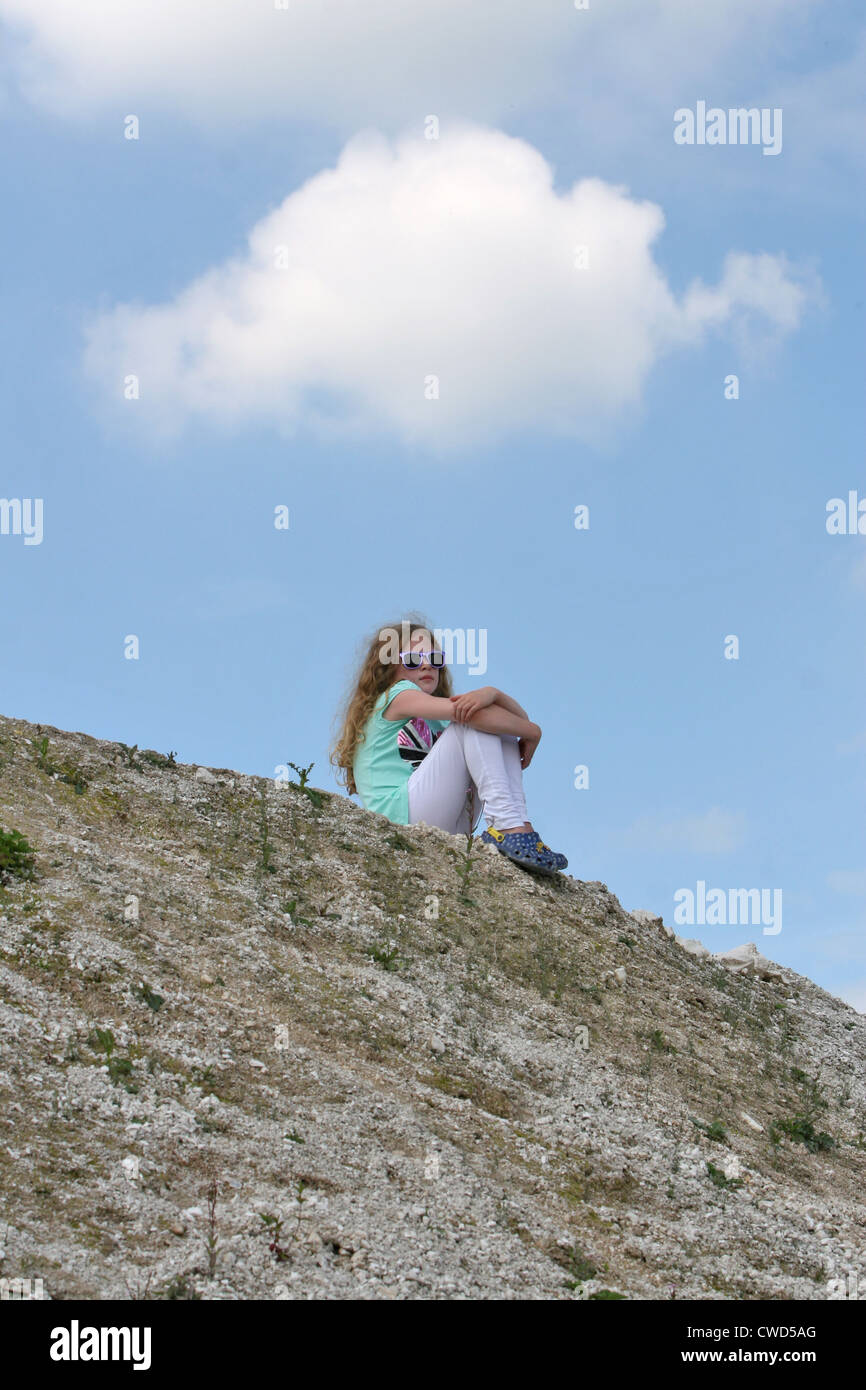 Blue Sky Denker: Ein junges Mädchen sitzt allein auf einem Hügel in Gedanken unter einem weißen Wolke. Stockfoto