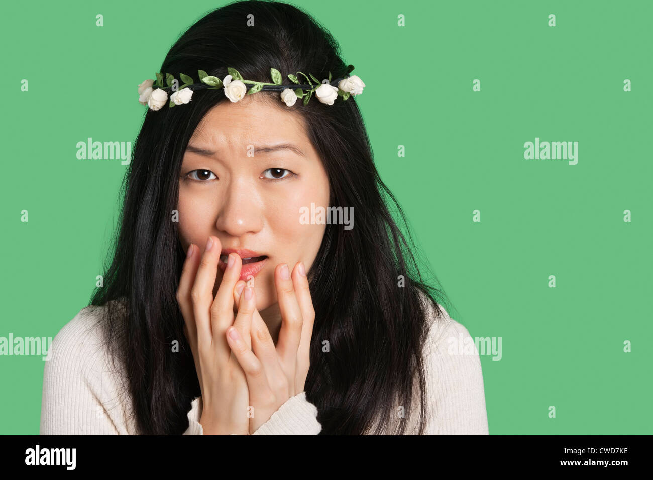 Porträt einer jungen Frau, die mit dem Ausdruck Furcht und Angst über grünen Hintergrund Stockfoto