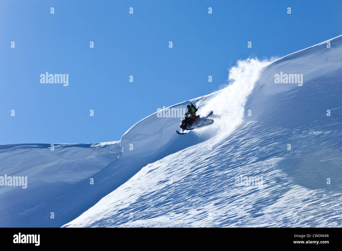 Ein Snowmobiler Sprung von einem Gesims an einem sonnigen Wintertag in Montana. Stockfoto