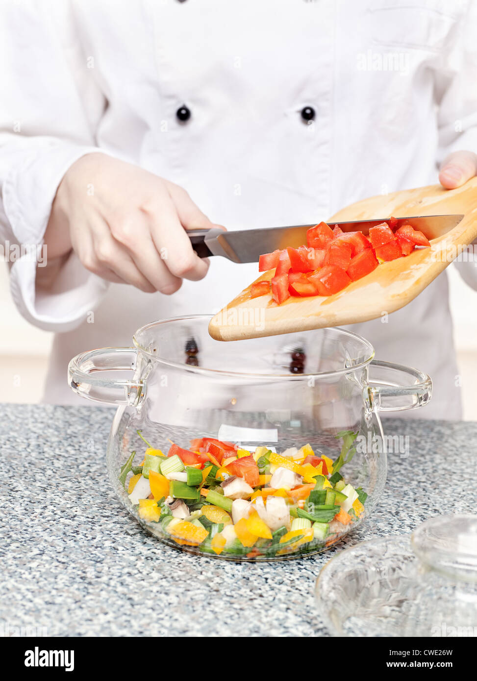 Koch fügt gehackte Tomaten in eine Glasschüssel mit anderem Gemüse Stockfoto
