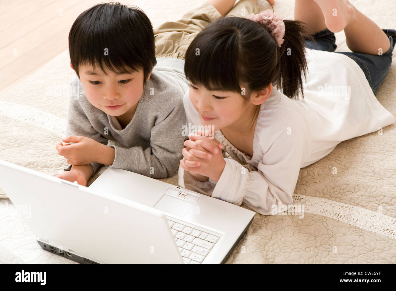 Zwei Kinder am Bauch liegen und Blick auf Laptop zusammen Stockfoto