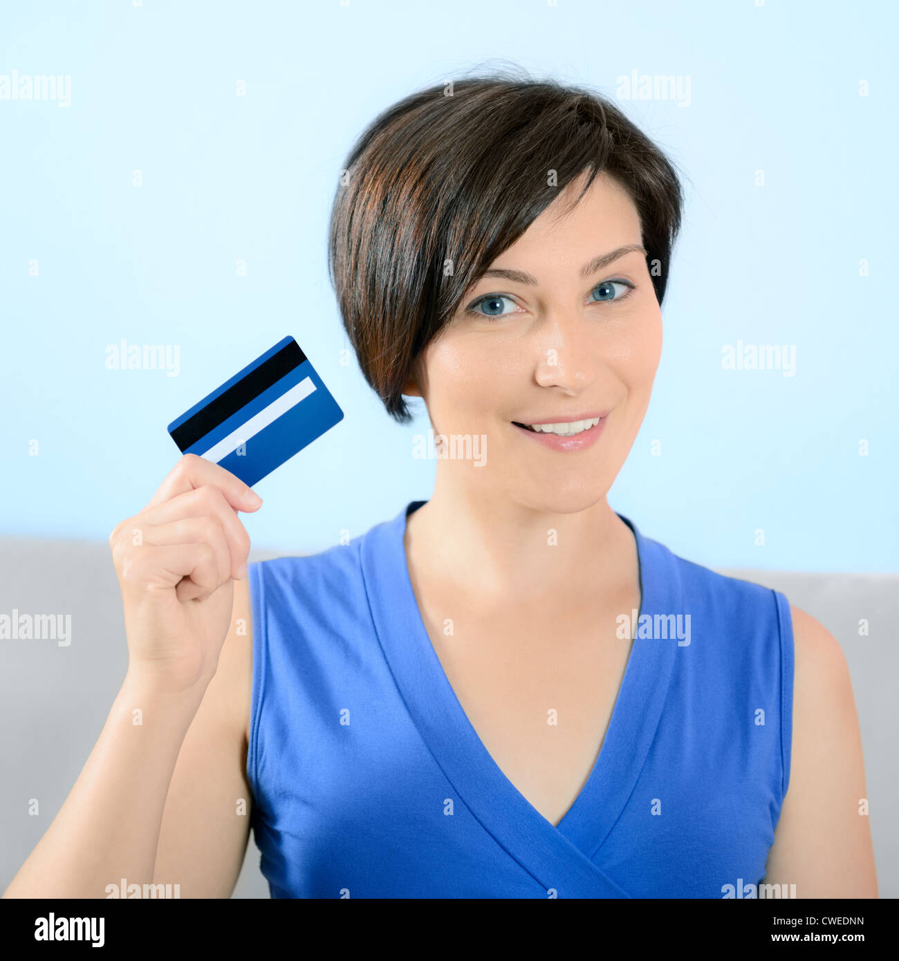 Hübsche junge Frau mit Lächeln auf dem Gesicht zeigt Kreditkarte. Stockfoto