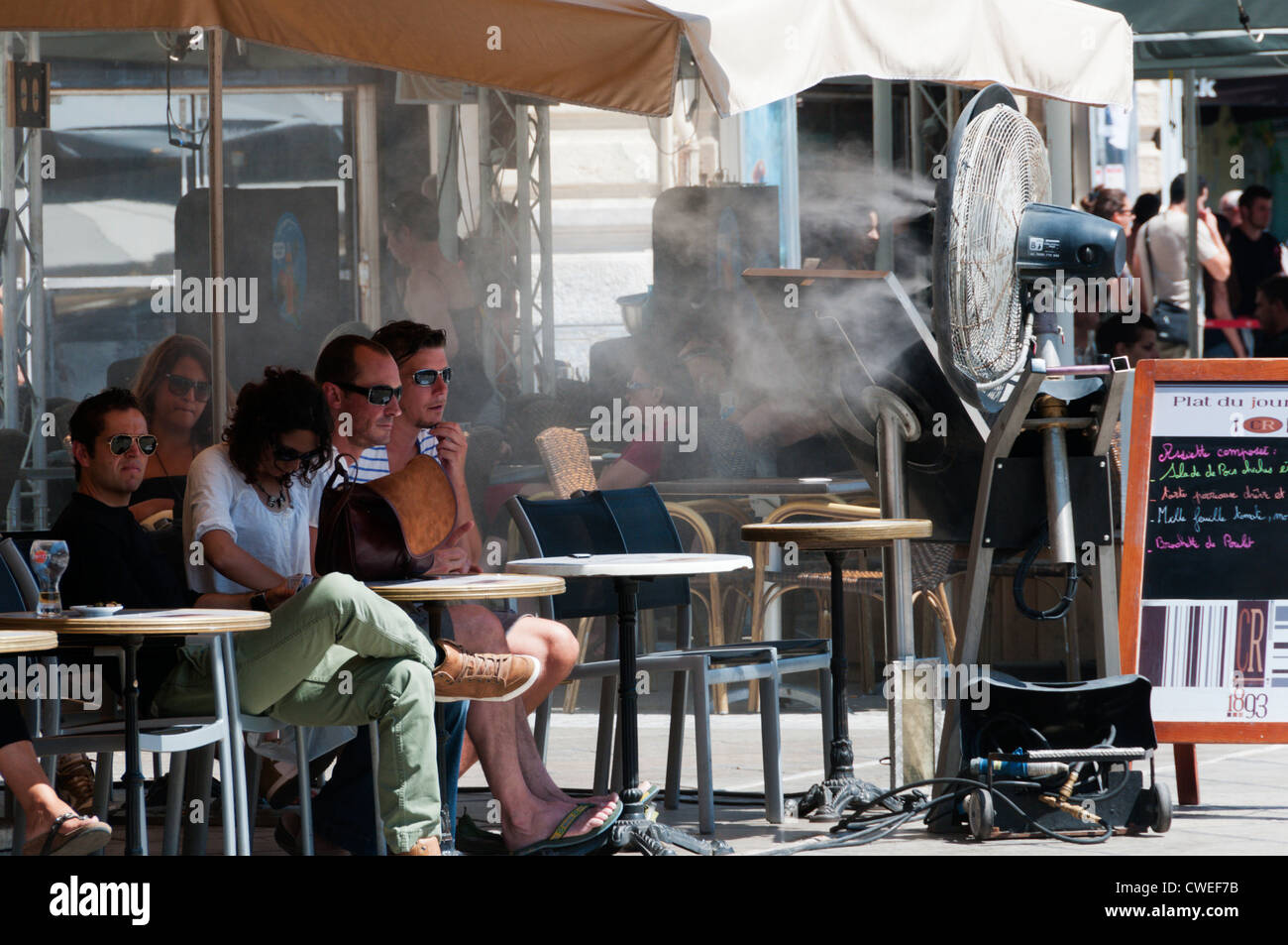 Kunden in einer Bar in die Place De La Comedie in Montpellier abkühlen vor eine große Fangemeinde mit einem kühlenden Nebel der Wasserstrahl Stockfoto