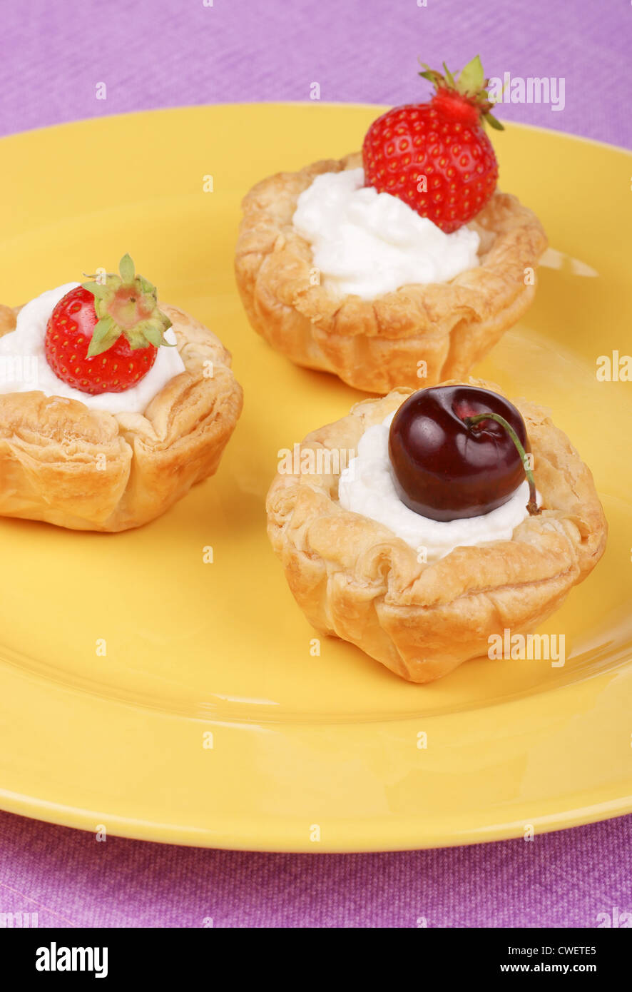 Kleine Törtchen mit Sahne, Erdbeeren und Kirschen auf dem gelben Silbertablett serviert Stockfoto
