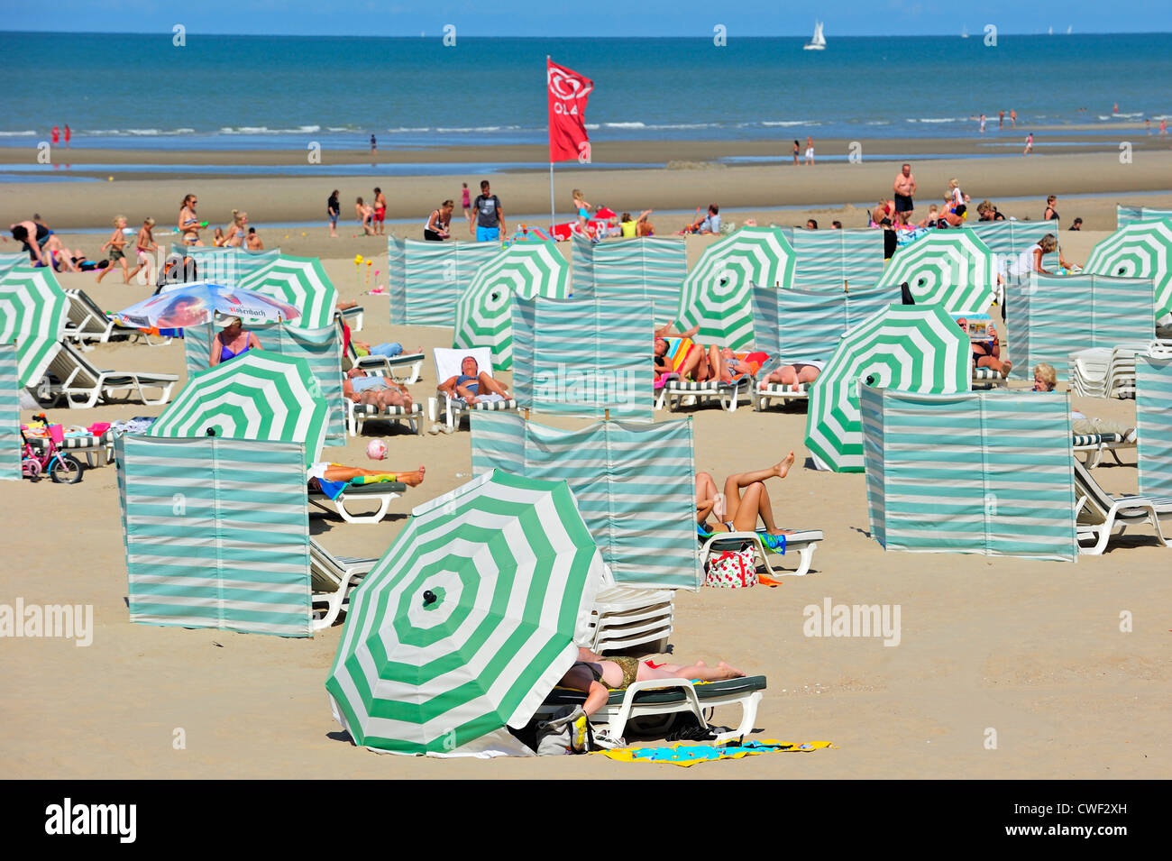Sonnenbaden im Sommer Sonnenbaden hinter Sonnenschirme und Windschutz am Strand entlang der Nordsee Küste in Koksijde / Coxyde, Belgien Stockfoto