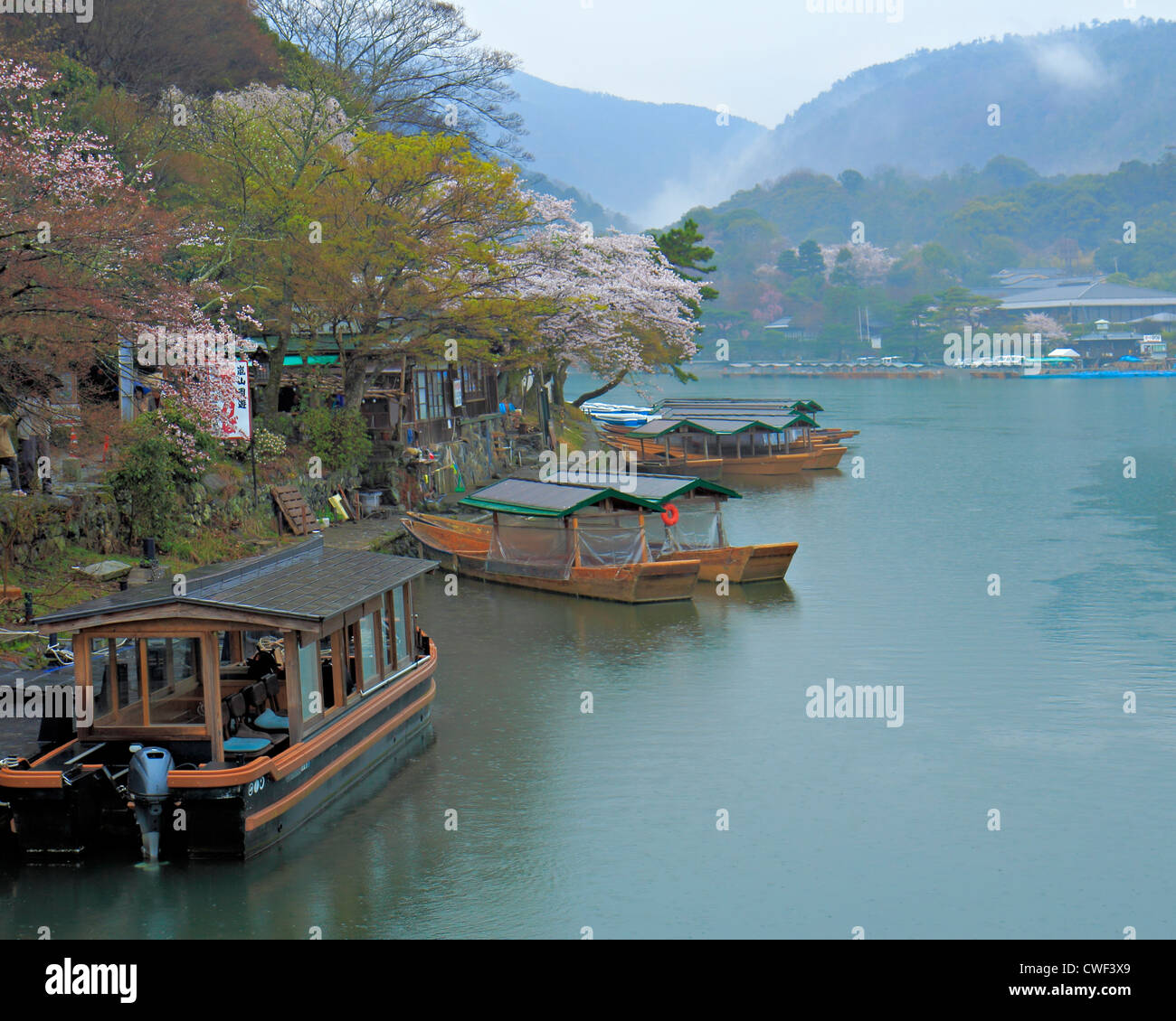 Flussufer mit traditionellen japanischen Boote und Kirschblüten mit bewaldeten Hügeln im Hintergrund Stockfoto