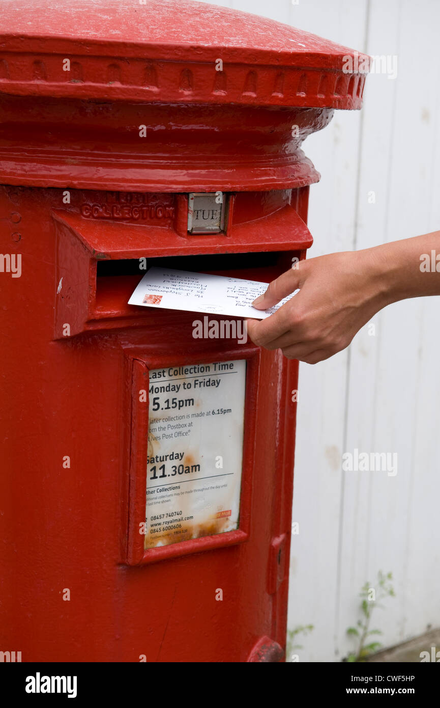 Person Posten oder mailing-Postkarten Urlaub in einen roten royal Mail-Briefkasten Stockfoto