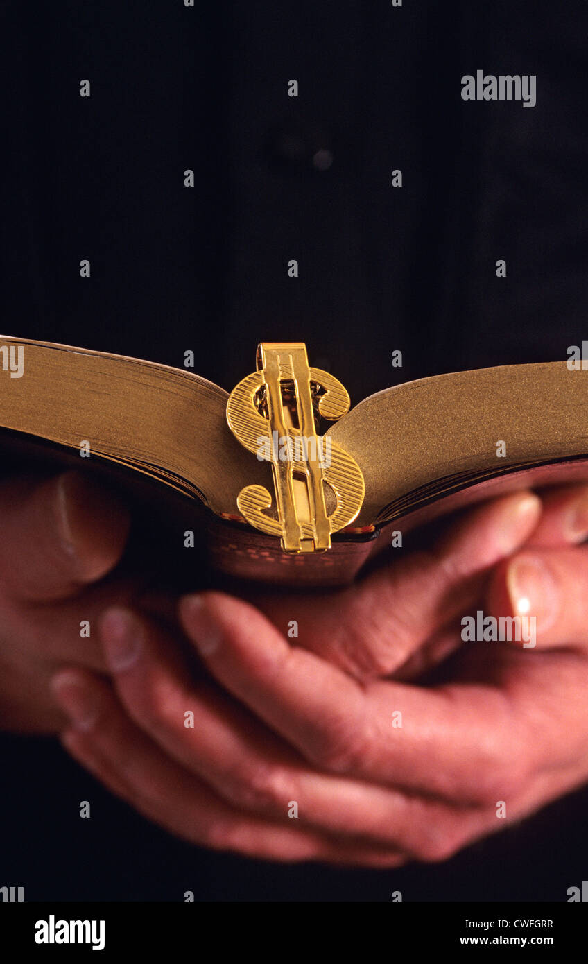 Mann, der Bibel mit einem Dollarzeichen Geldscheinklammer Kennzeichnung der Seite hält Stockfoto