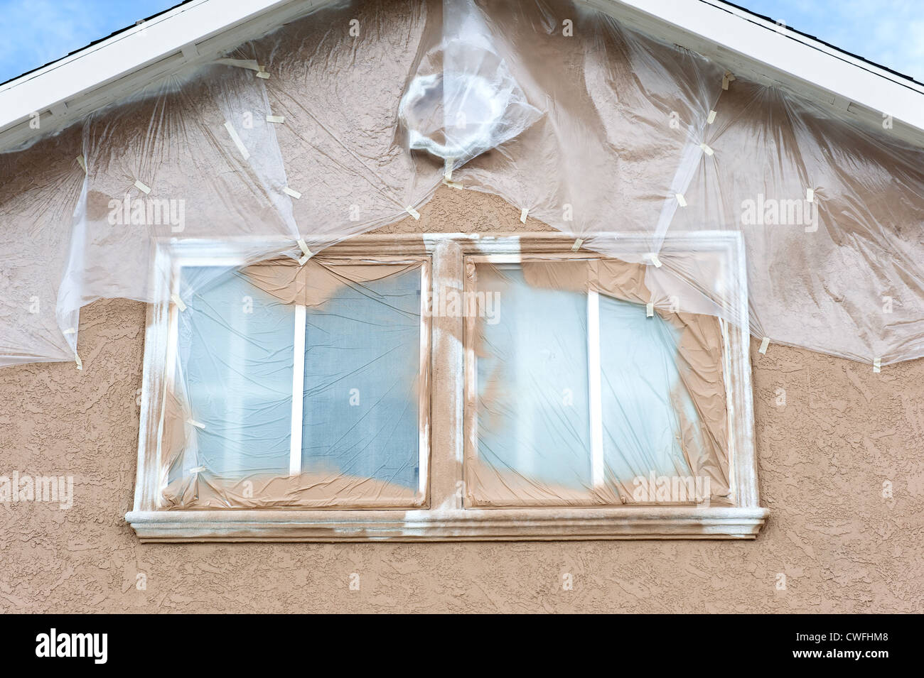 Ein Haus wird neu gestrichen werden und ist sorgfältig mit Plastikplanen zum Schutz der Gebiete von Lacknebel maskiert Stockfoto