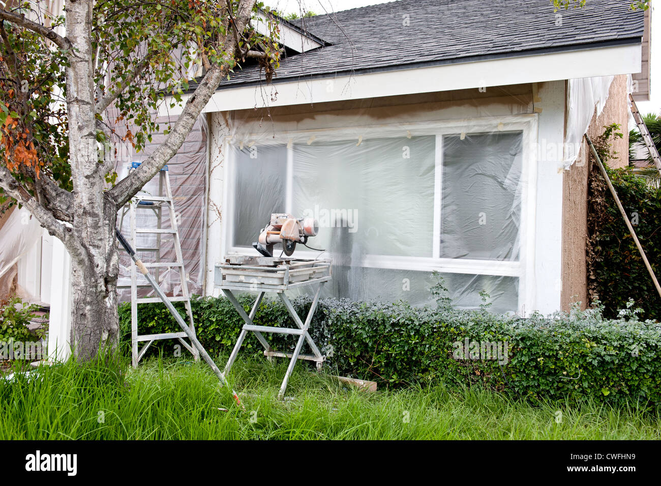 Eine Fliese Säge und Leiter vor einem Kunststoff bedeckt Fenster in ein Haus renovieren. Stockfoto