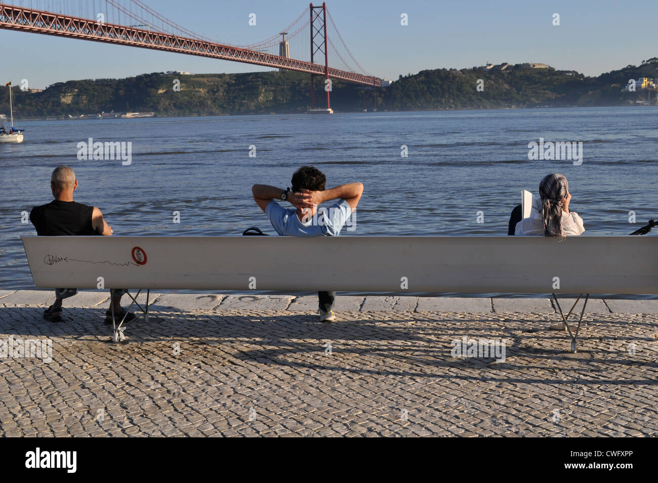 Leute sitzen auf Bank durch den Fluss Tejo in Lissabon, Portugal Stockfoto