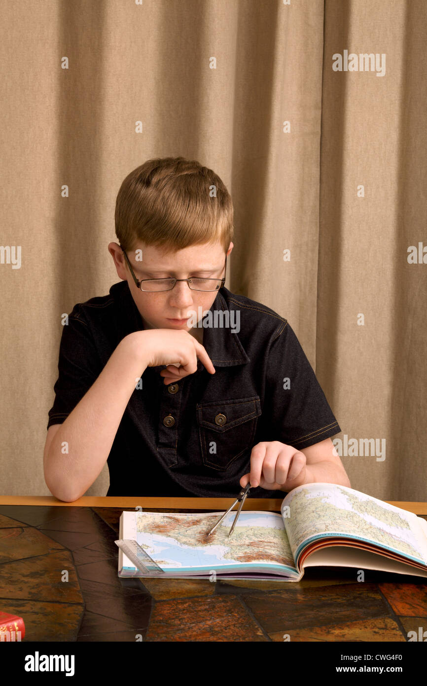 Ein 12 Jahre alter Junge verwendet, Trennwände, Abstand auf einer Karte in einem Atlas zu prüfen. Stockfoto