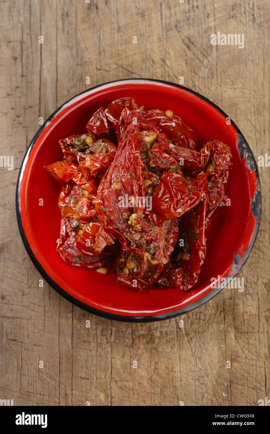 sonnengetrocknete Tomaten mit Olivenöl in roten Emaille Schüssel, alten Holztisch Stockfoto