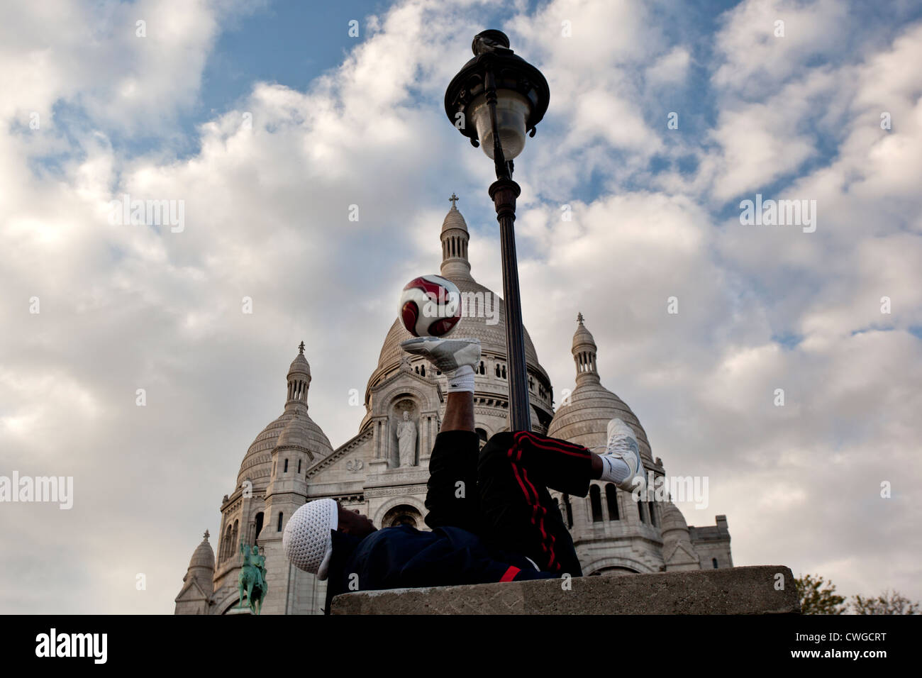 Ein junger Mann liegt auf dem Rücken und dabei einen Fußball in der Luft mit den Füßen auf den Stufen von der Sacre Coeur, Paris. Stockfoto