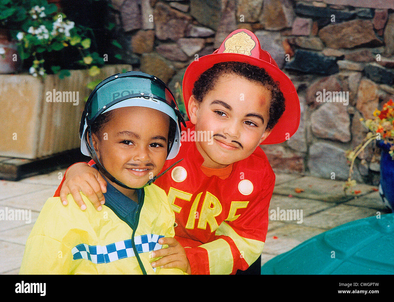 Kinder draußen im Garten. Zwei Jungen gekleidet - als Feuerwehrmann und Polizist. Stockfoto