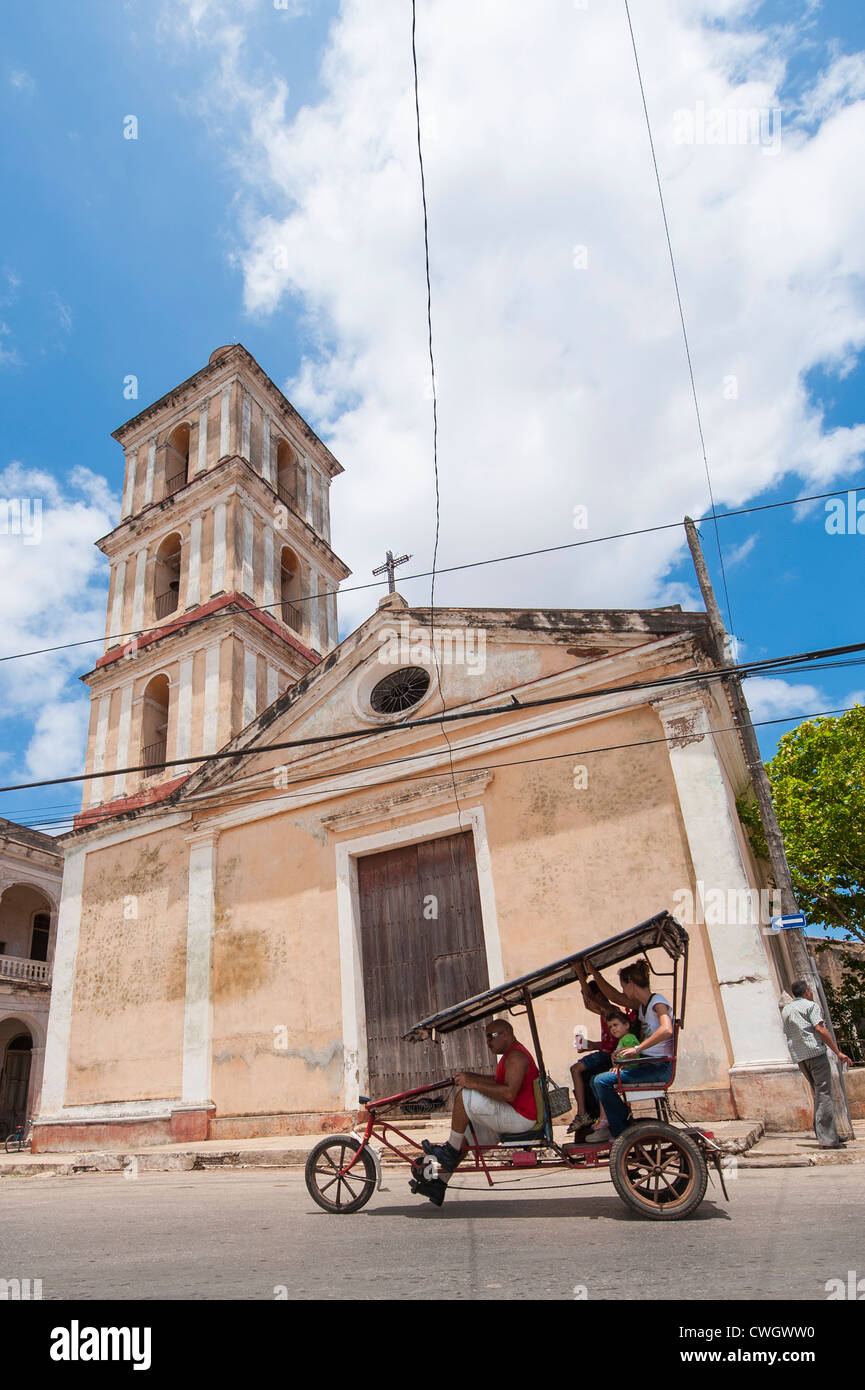Leute Reiten Dreirad taxi vor Iglesia del Buen Viaje katholische Kirche, Remedios, Kuba. Stockfoto