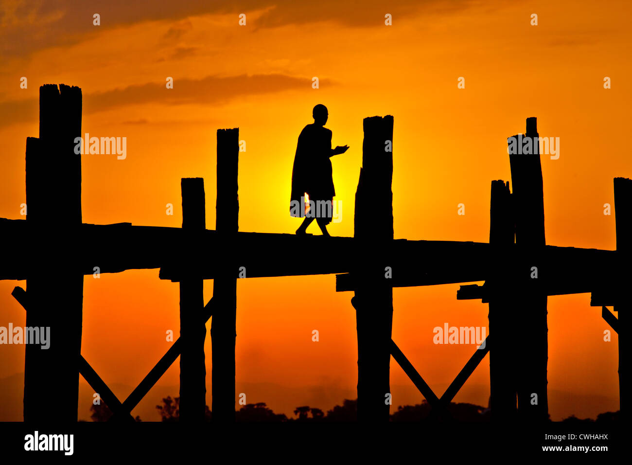 Die BURMESISCHEN Mönch nutzt das Teakholz U KLANGKUNST Brücke Pendeln über den Taungthaman-See bei Sonnenaufgang - AMARAPURA, MYANMAR Stockfoto