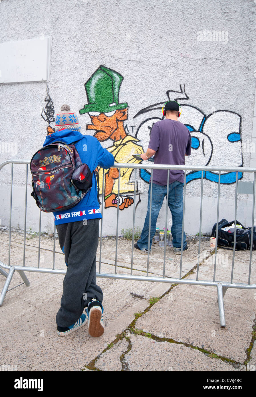 Teenager beobachten Graffitikünstler sprühen seine Wandstück Stockfoto