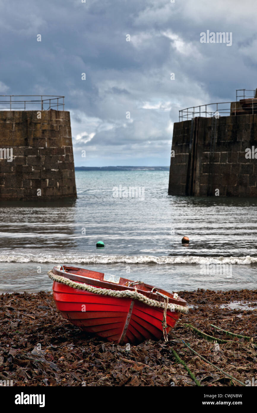 Ein kleine rote hölzernen Fischerboot vor Anker im Hafen von Mousehole Cornwall mit Gewitterwolken am Horizont. Stockfoto