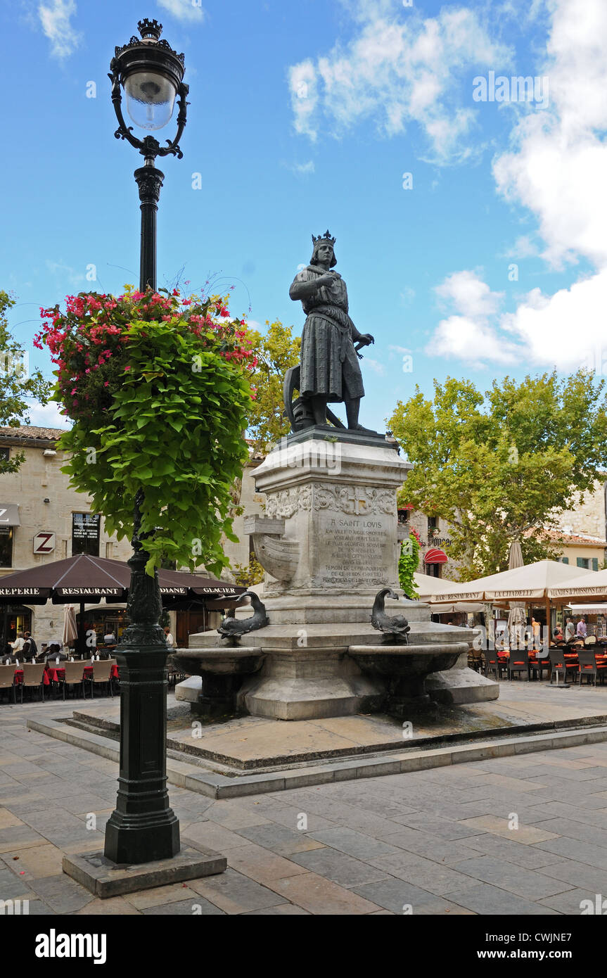 Statue von Saint St Louis in Ort St Louis Aigues Mortes Frankreich mit reich verzierten gusseisernen Lamp Post Blumenkörbe und Markt Stände Stockfoto