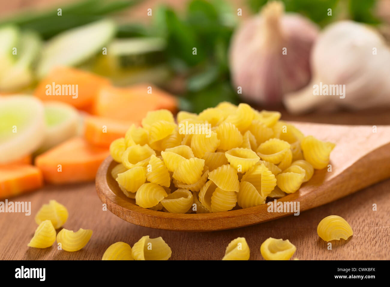 Rohe Schale Nudeln oder Conchiglioni auf Holzlöffel mit rohem Gemüse (Karotten, Lauch, Zucchini, Knoblauch) in den Rücken Stockfoto