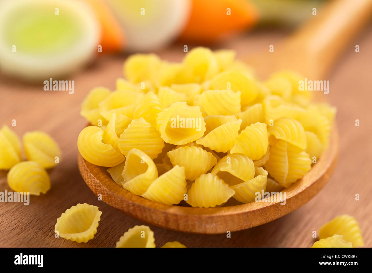 Rohe Schale Nudeln oder Conchiglioni auf Holzlöffel mit rohen Gemüse (Karotten und Lauch) in den Rücken Stockfoto