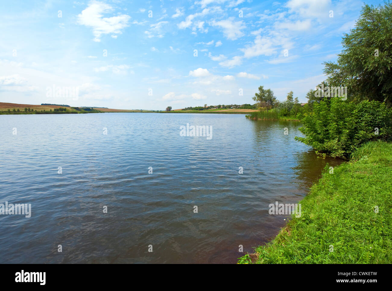 Sommer rushy Seeblick mit Dorf am gegenüberliegenden Ufer Stockfoto