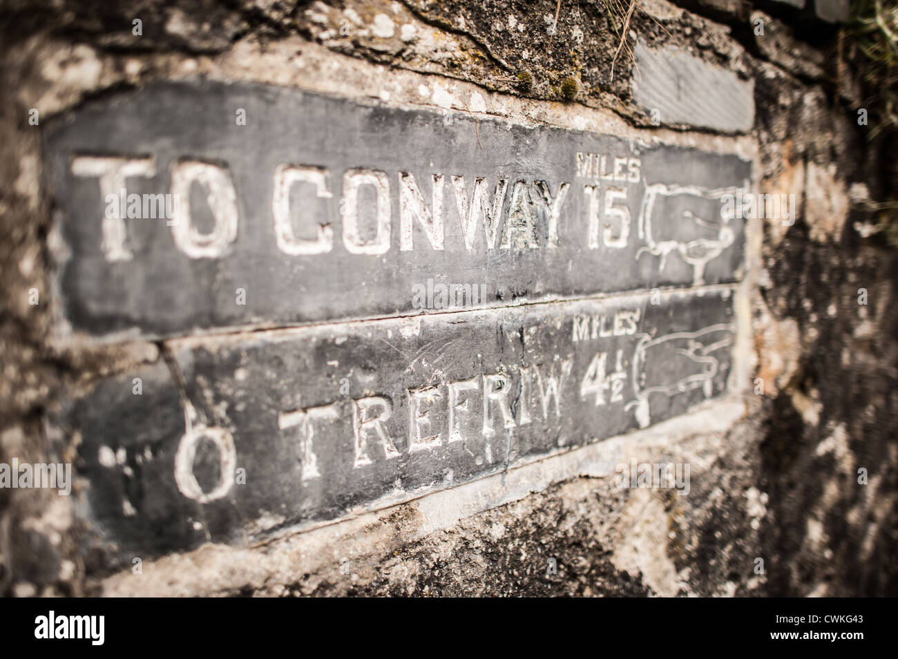 Betws-y-Coed StraßenSzene Conwy Tal Wales | BETWS-Y-COED, Vereinigtes Königreich — Ein verwitterter Steinmeilenstein mit der Aufschrift „NACH CONWAY 15“ und „NACH TREFRIW 4½“ Meilen markiert die Routen durch dieses Snowdonia-Dorf mit etwa 564 Einwohnern. Betws-y-Coed wurde nach David Cox, der hier ab 1844 den Sommer verbrachte, zu einem Magneten für Landschaftsmaler; ein Kreis, dem später die Gründung der ersten Künstlerkolonie Großbritanniens zugeschrieben wurde. Das Dorf liegt im Eryri (Snowdonia) Nationalpark an der Mündung der Flüsse Conwy und Llugwy. Stockfoto