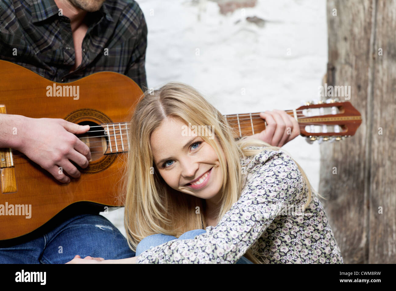 Frau, Lächeln, Mann spielt Gitarre im Hintergrund Stockfoto