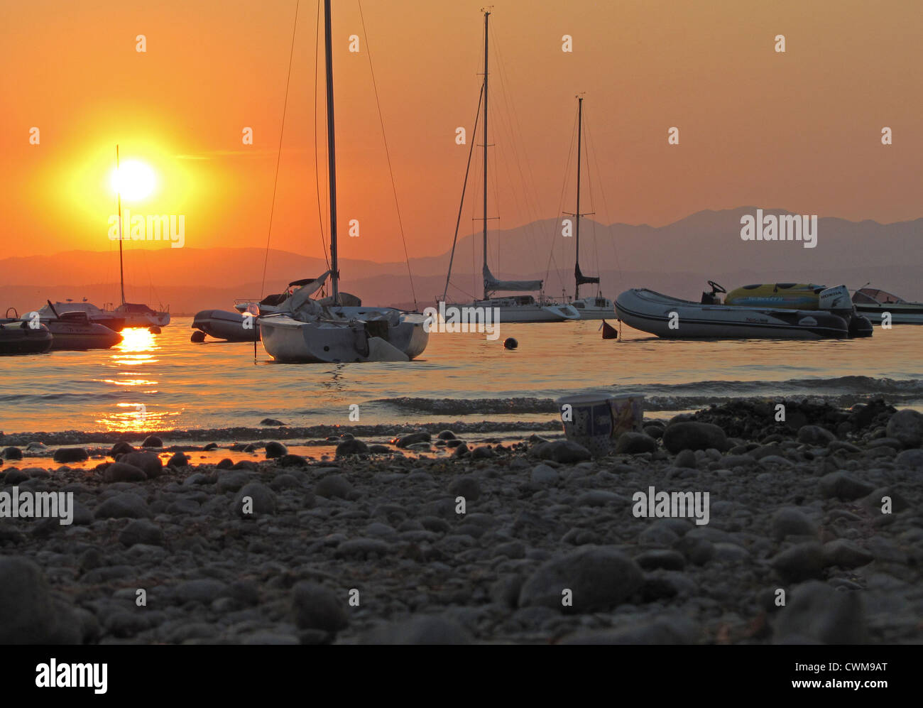 Steiniger Strand, Gardasee bei Sonnenuntergang, Camping Lido, Pacengo, Italien, mit festgemachten Boote im Hintergrund Stockfoto