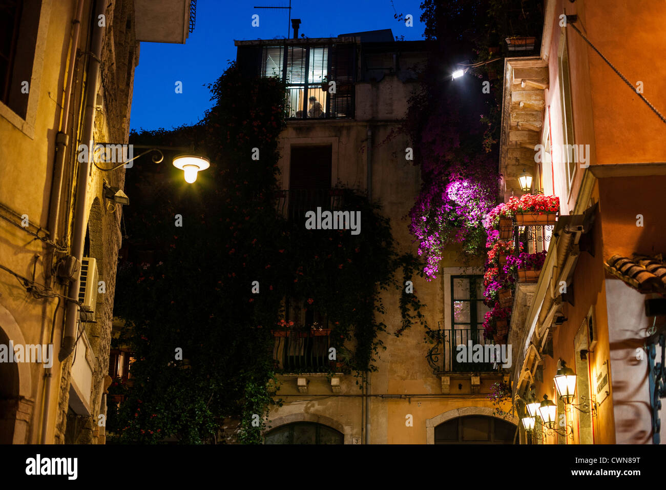 Eine Frau, die Silhouette in einem Fenster im oberen Stock in einer Seitenstraße von Taormina, Sizilien Stockfoto