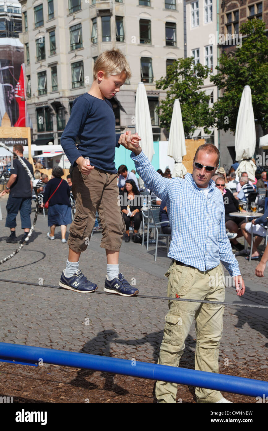 Junge balancing und Seil gehen auf einem Draht mit einem festen Griff in der Hand seines Vaters in der Fußgängerzone Stroeget (Strøget), Kopenhagen Stockfoto