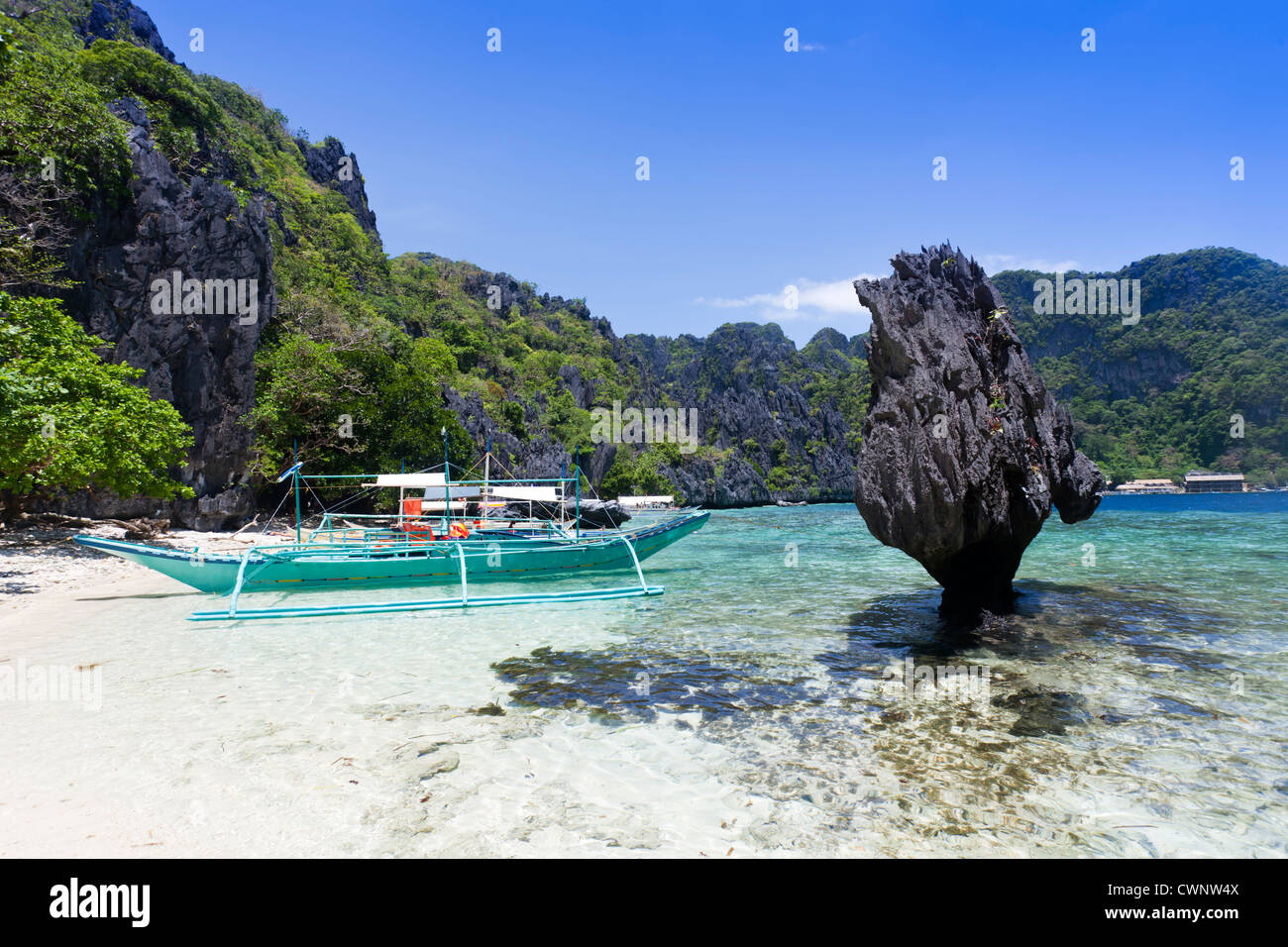 Einsames Boot, dunklen Felsen, blaues Meer und Himmel, weißer Strand, El Nido, Palawan, Philippinen. Stockfoto