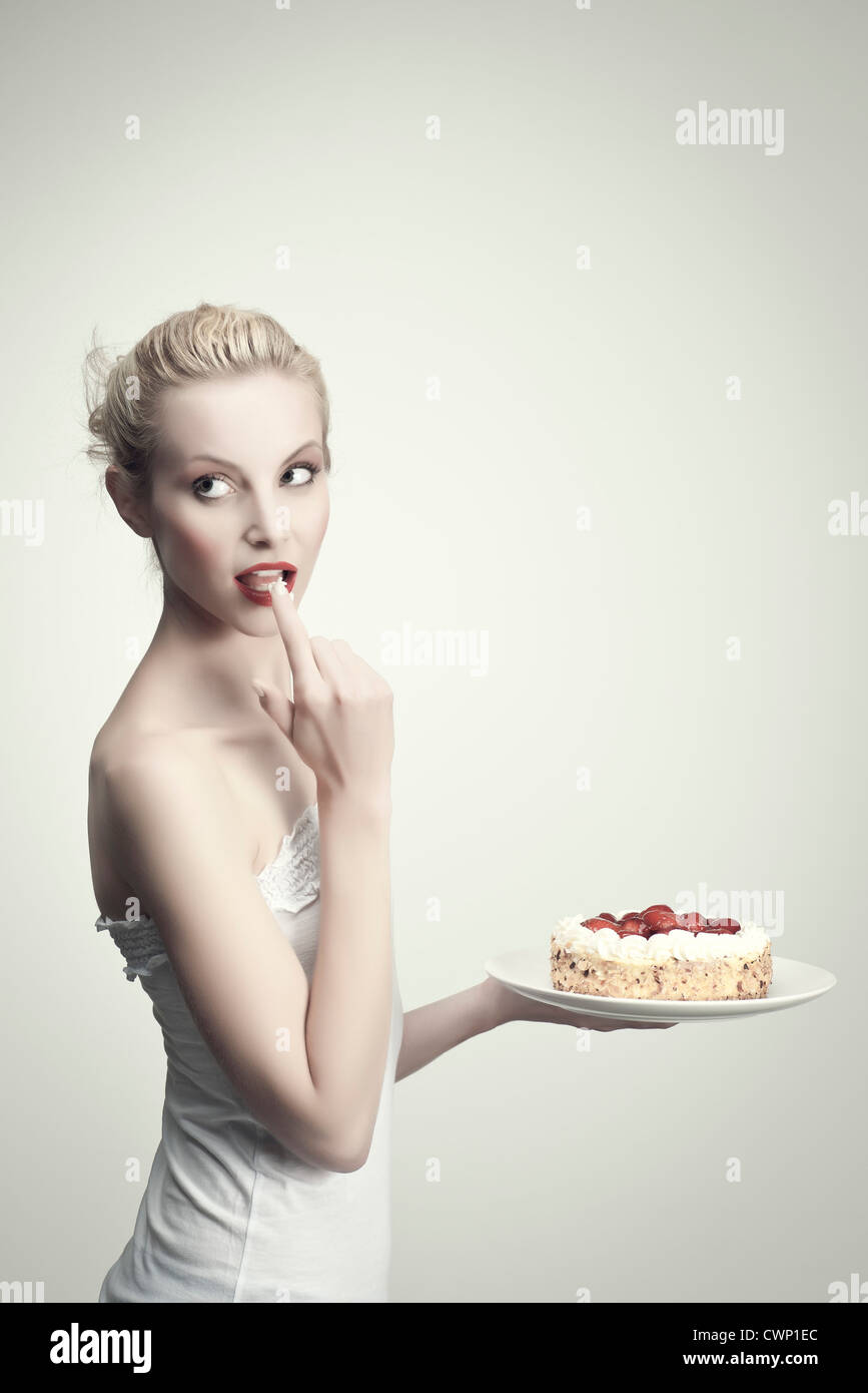 Junge Frau mit Erdbeerkuchen, leckt Sahne von Finger, Porträt Stockfoto