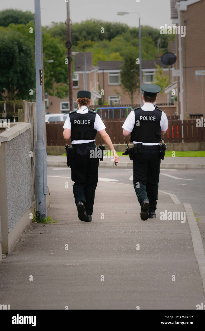 Weibliche und männliche Polizisten zu Fuß auf dem Gehweg einer Straße in einem Wohngebiet (Vignettierten) Stockfoto