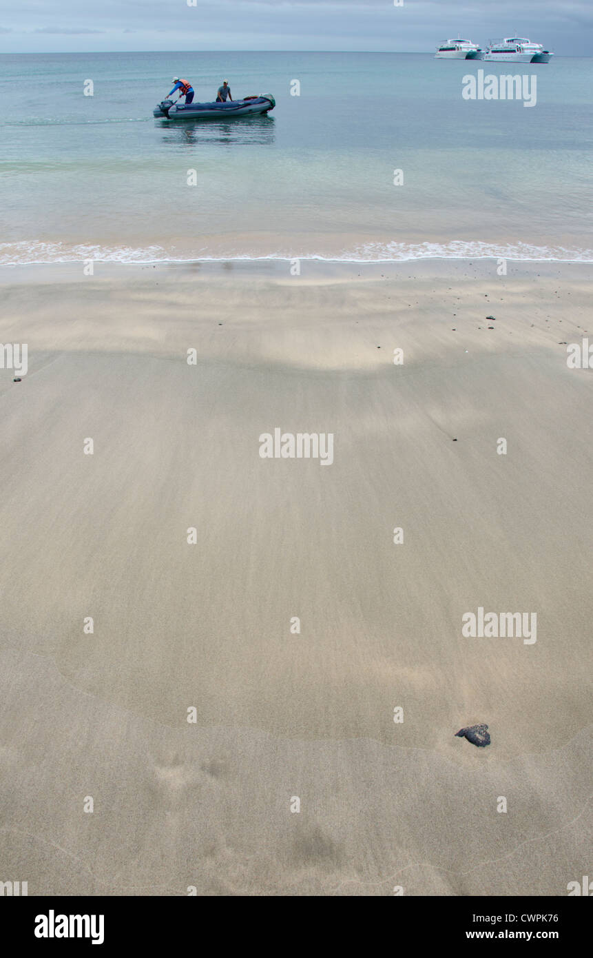 Ecuador, Galapagos, Floreana, Punta Cormoran. Wellenmuster am Sandstrand mit touristischen Yachten in Ferne. Stockfoto