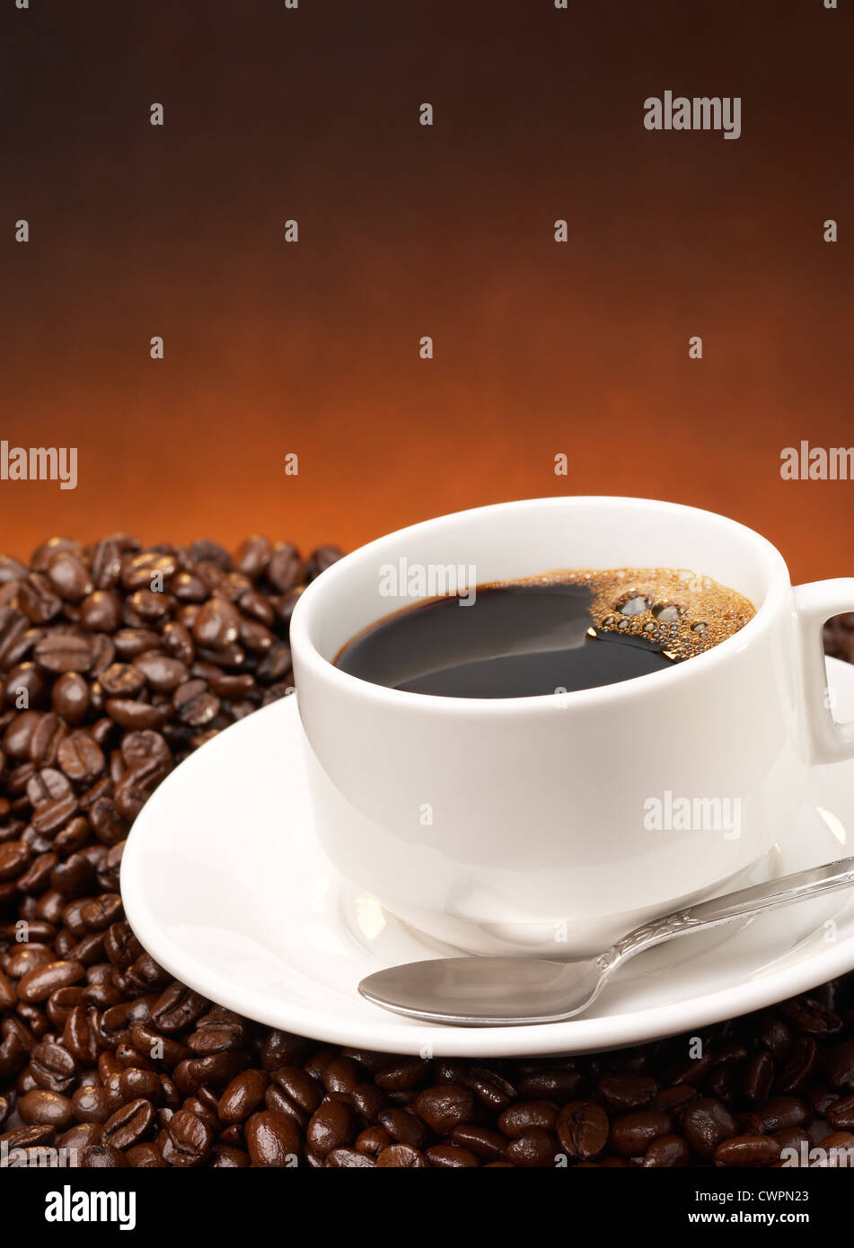 schwarze Tasse mit Untertasse und Löffel auf Kaffeebohnen Stockfoto