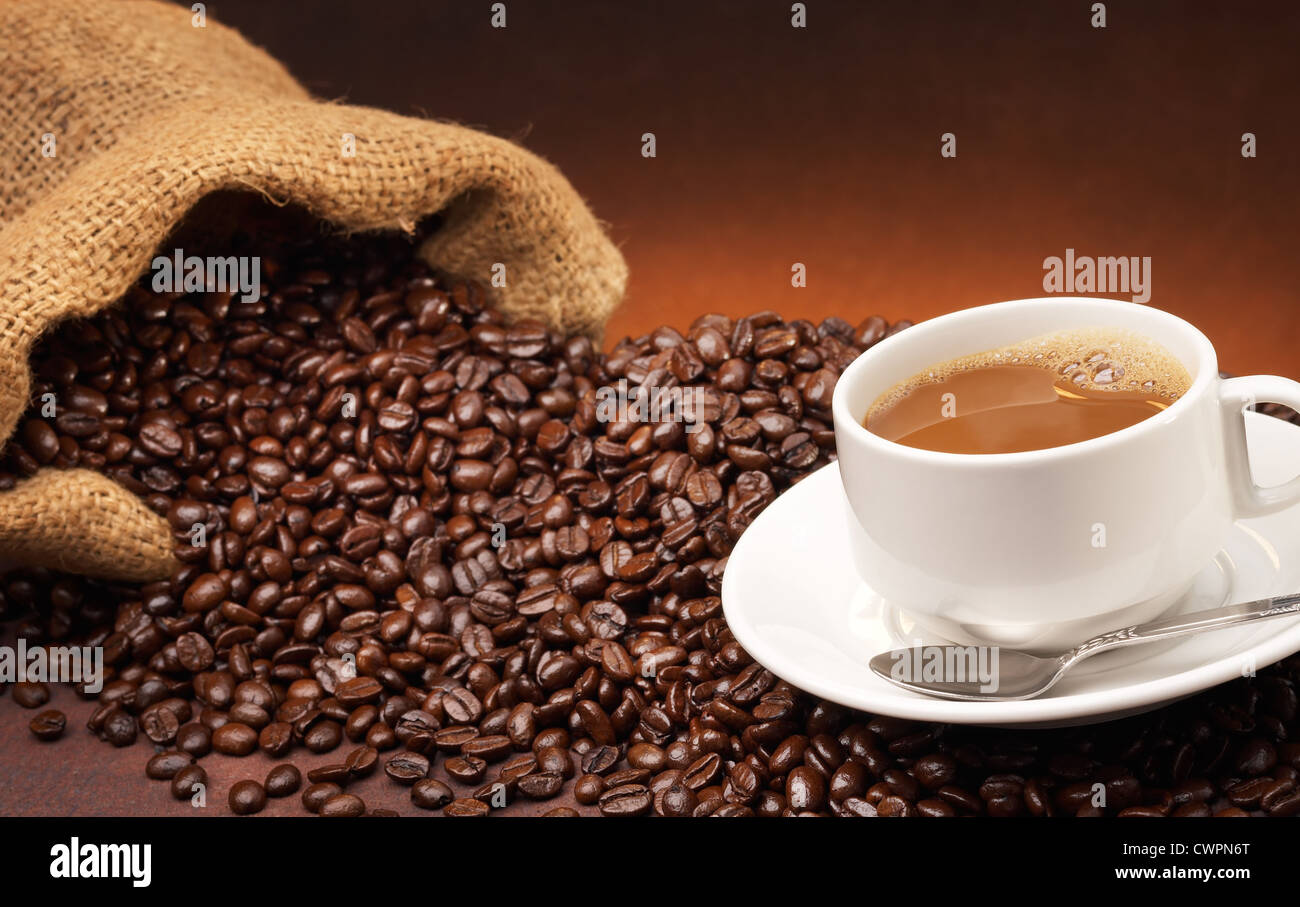 Tasse mit Untertasse und Löffel auf Kaffeebohnen Stockfoto