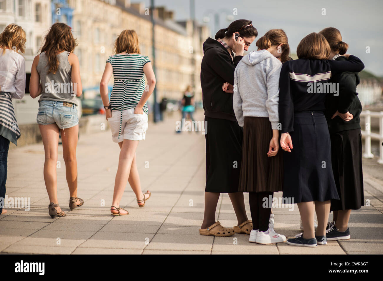 Kulturelle Unterschiede: eine Gruppe von orthodoxen jüdischen Mädchen im Sommerurlaub in Aberystwyth, mit drei Jugendliche tragen shorts UK Stockfoto